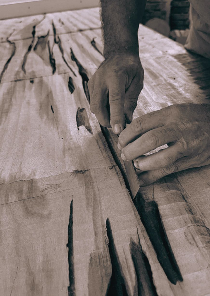 Mãos do artesão da Körber Art & Design trabalhando uma prancha de madeira de veios escuros, em preto e branco